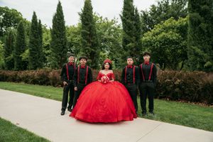 An outdoor quinceañera photo session with attendants walking along a garden path.