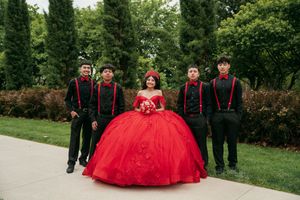 A formal group portrait featuring black attire and a striking red ball gown in a garden setting.