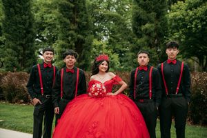 A group wearing black suits with red accents poses outdoors in a garden setting for a formal event.