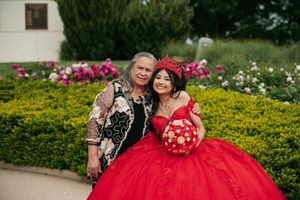 A vibrant red quinceañera dress stands out against colorful garden flowers and greenery.