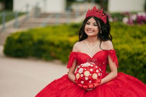 Stunning red quinceañera dress with intricate beading and floral details in an outdoor garden setting.
