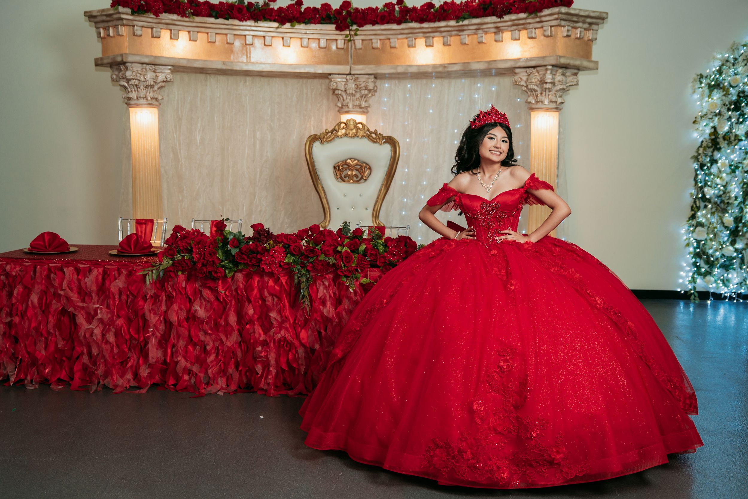A stunning red quinceañera ball gown with intricate beading and a full tulle skirt in an elegant ballroom setting.