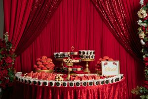 Red sequin backdrop with dessert display tables featuring cupcakes and treats at an elegant event.