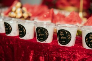 White candles with black and gold labels displayed on a luxurious red velvet tablecloth.