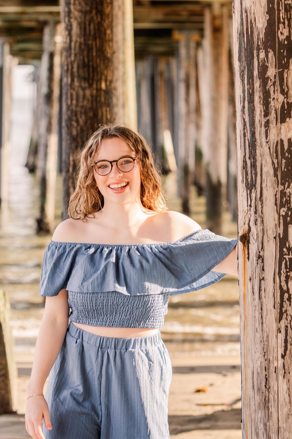 A series of photos under wooden pier posts showing a blue off-shoulder top against natural lighting.