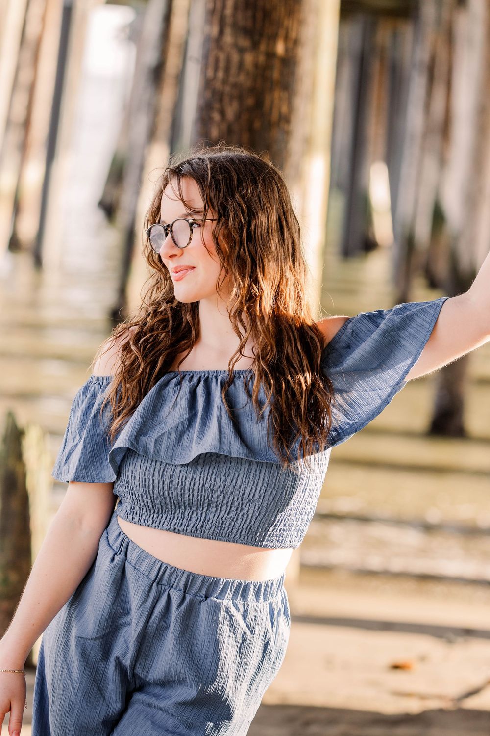 Natural light portrait by wooden pier wearing blue off-shoulder crop top and matching bottoms.