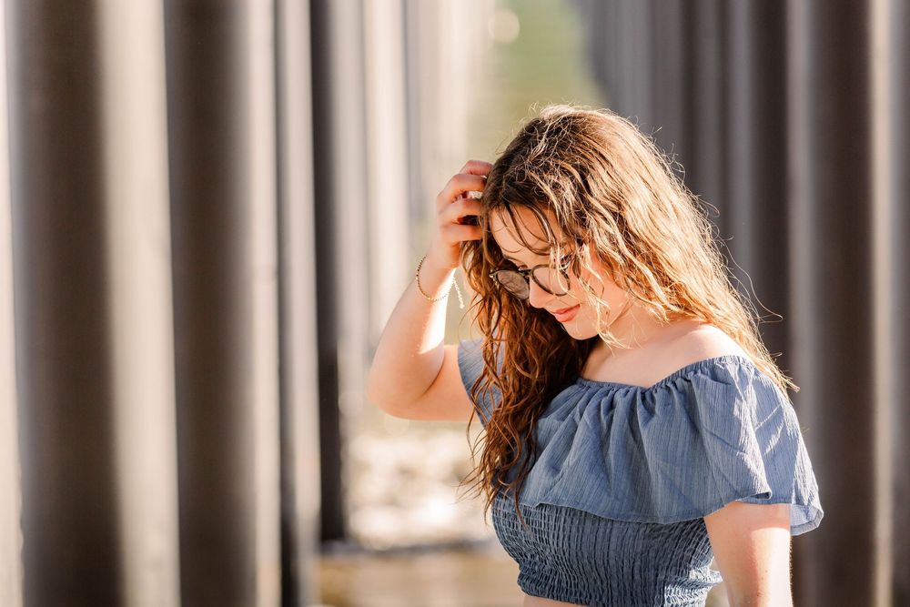 Woman in blue dress walking through an elegant colonnade with sunlight streaming between pillars.