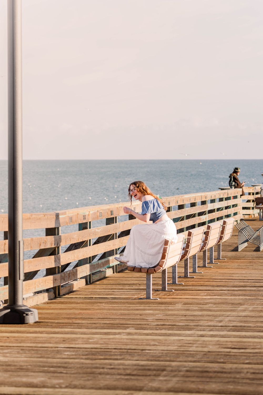 White clothing hangs on a wooden pier railing overlooking the ocean on a sunny day.