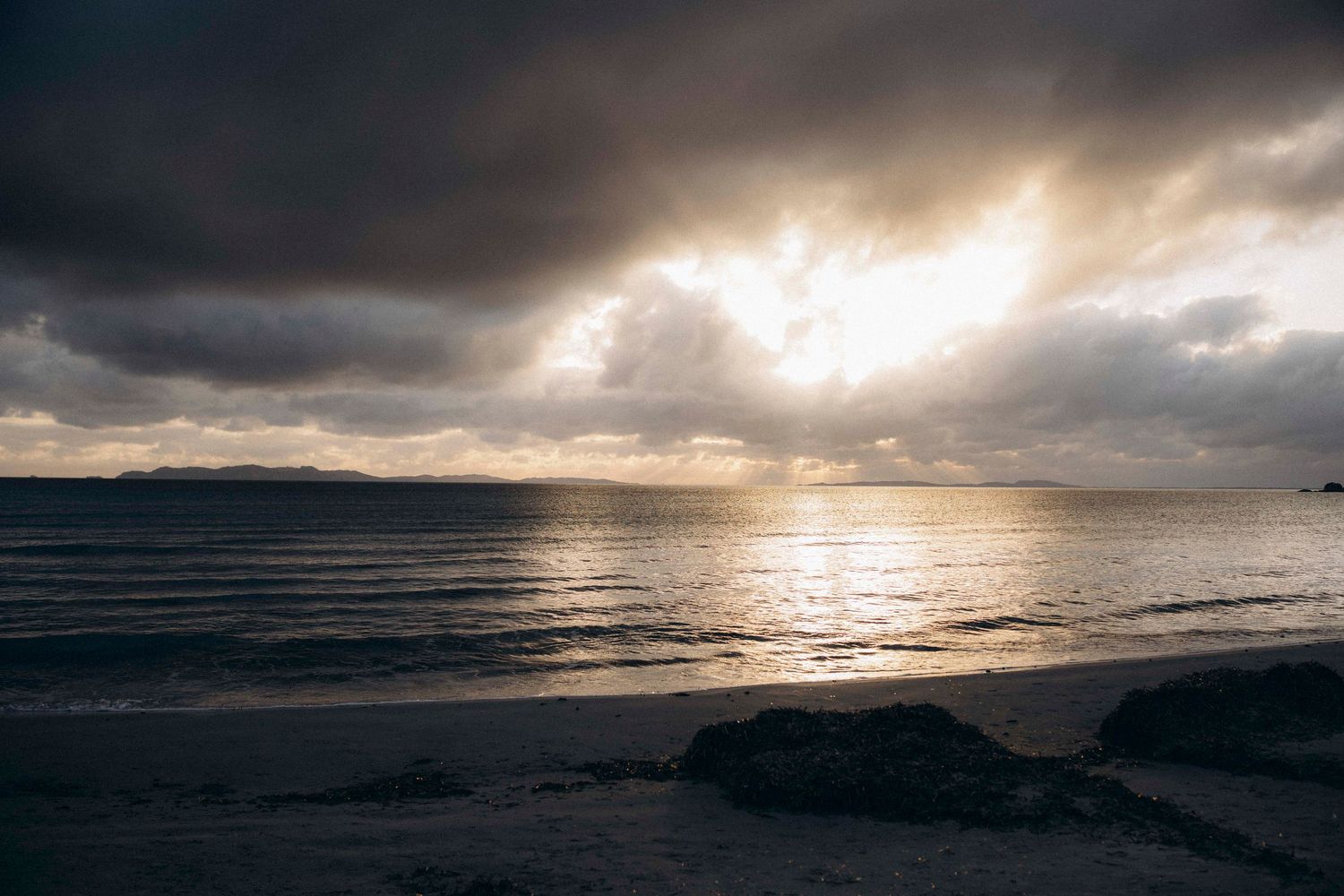 Dramatic ocean sunset with sunbeams piercing through dark storm clouds over the horizon.