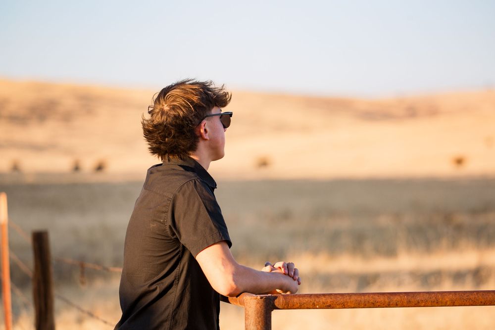 Person sits on a wooden railing overlooking a vast desert landscape during sunset.