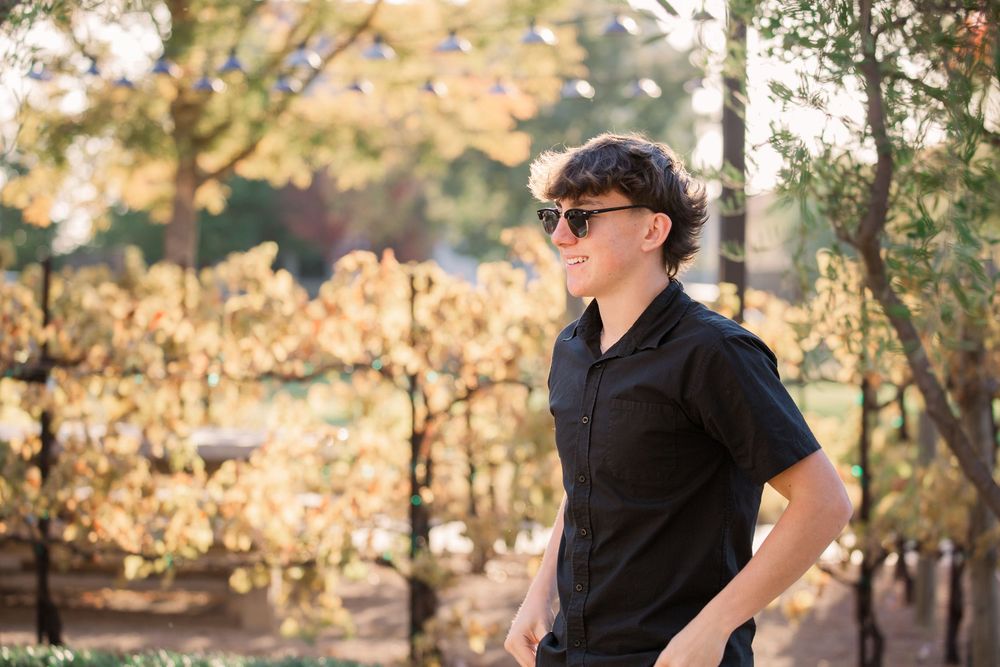 A person in black attire sits on a wooden bench in an autumn park setting with golden leaves in the background.