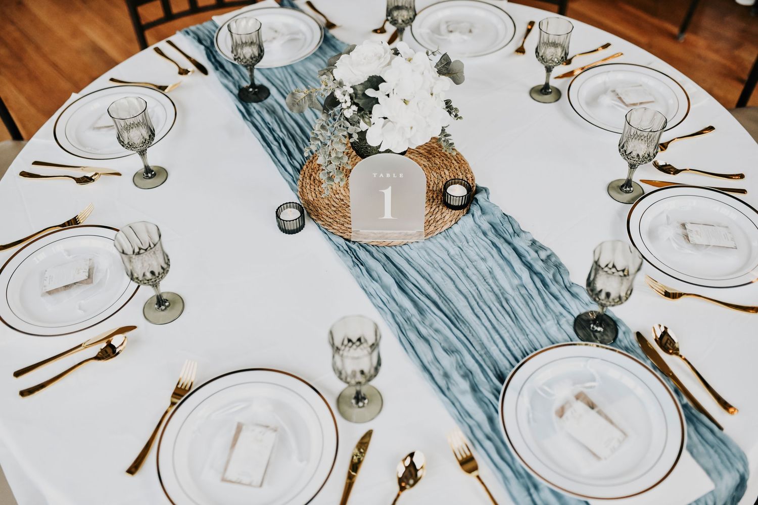 Wedding table details with powder blue and gray vintage goblets, gold flatware, and ivory plates