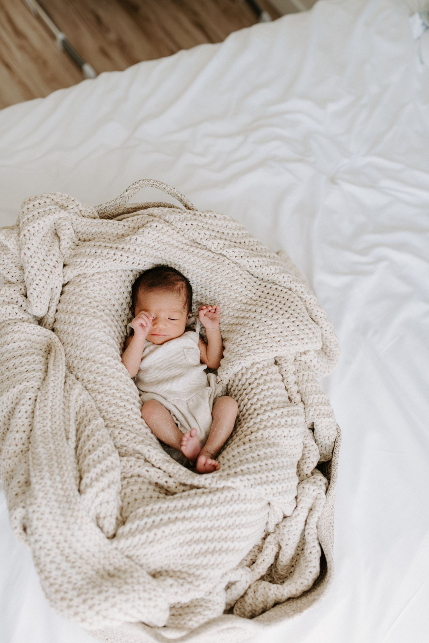 Newborn sleeping peacefully wrapped in cream knit blanket on white bedding.