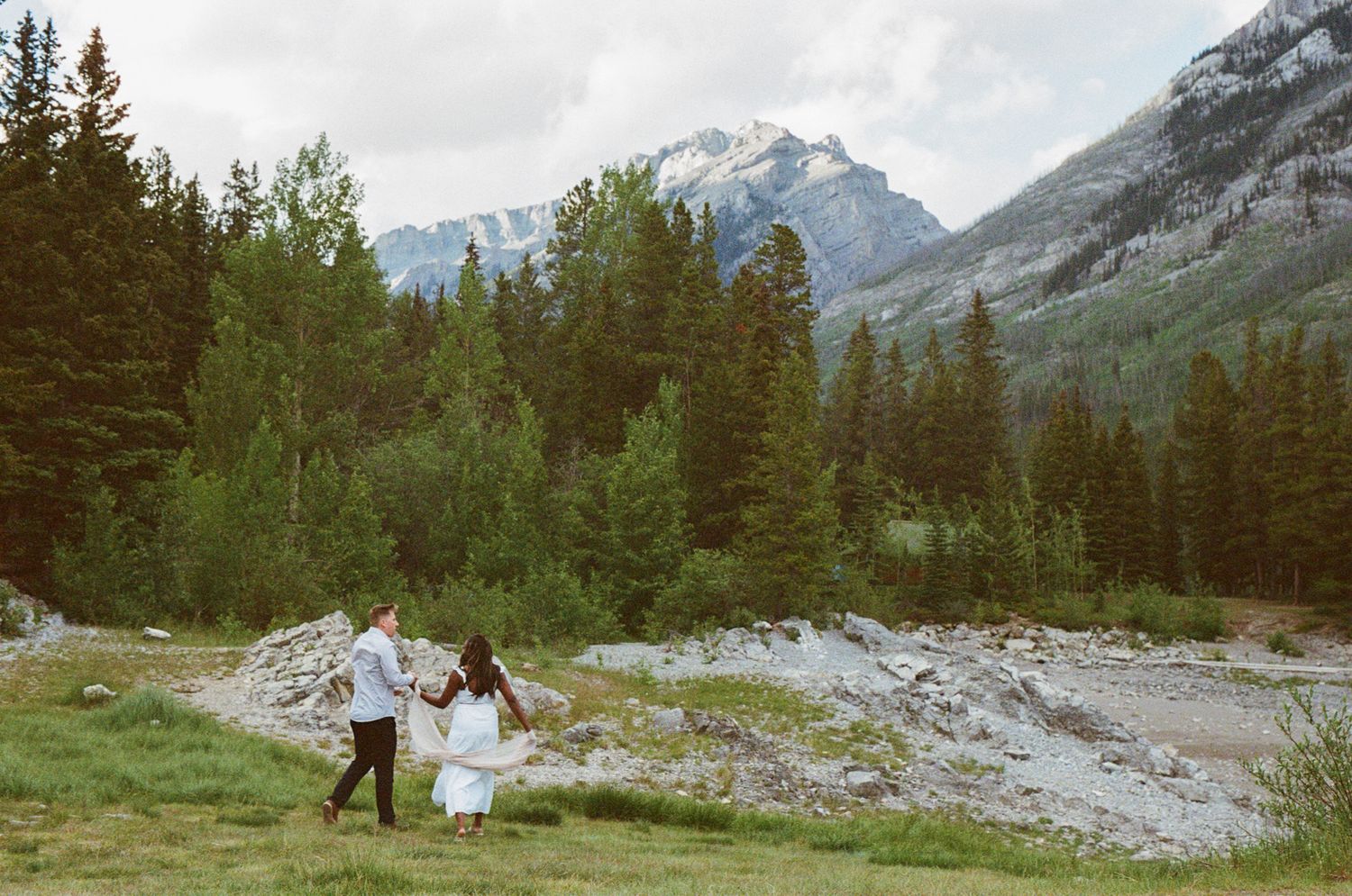 bride and groom wander through a field on the edge of a mountain lake in Kananaskis