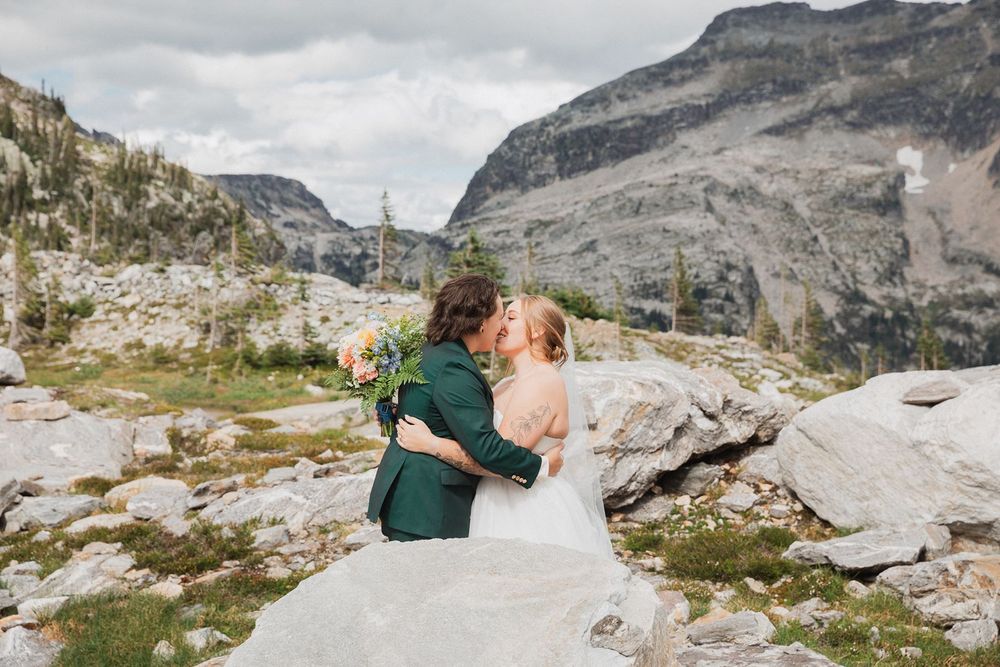 Couple kisses in front of rocky mountain landscape during outdoor wedding ceremony.