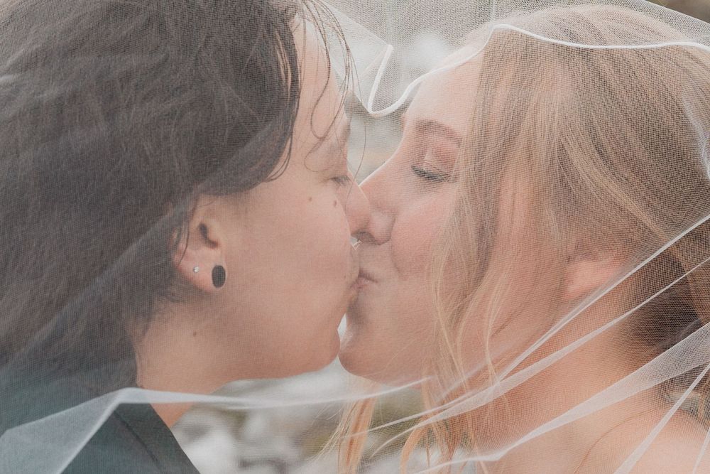 Bride and partner share intimate kiss under wedding veil in close-up portrait.