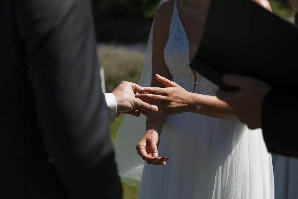 Groom placing wedding ring on bride's finger during outdoor ceremony.