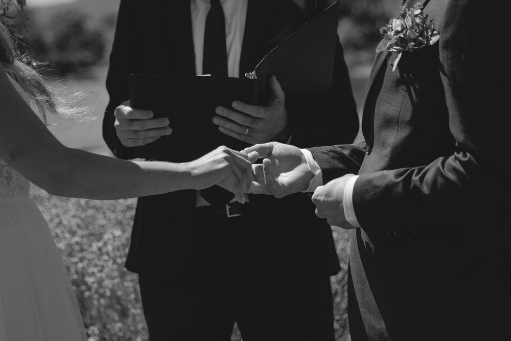 Black and white photo of couple exchanging rings at wedding ceremony.