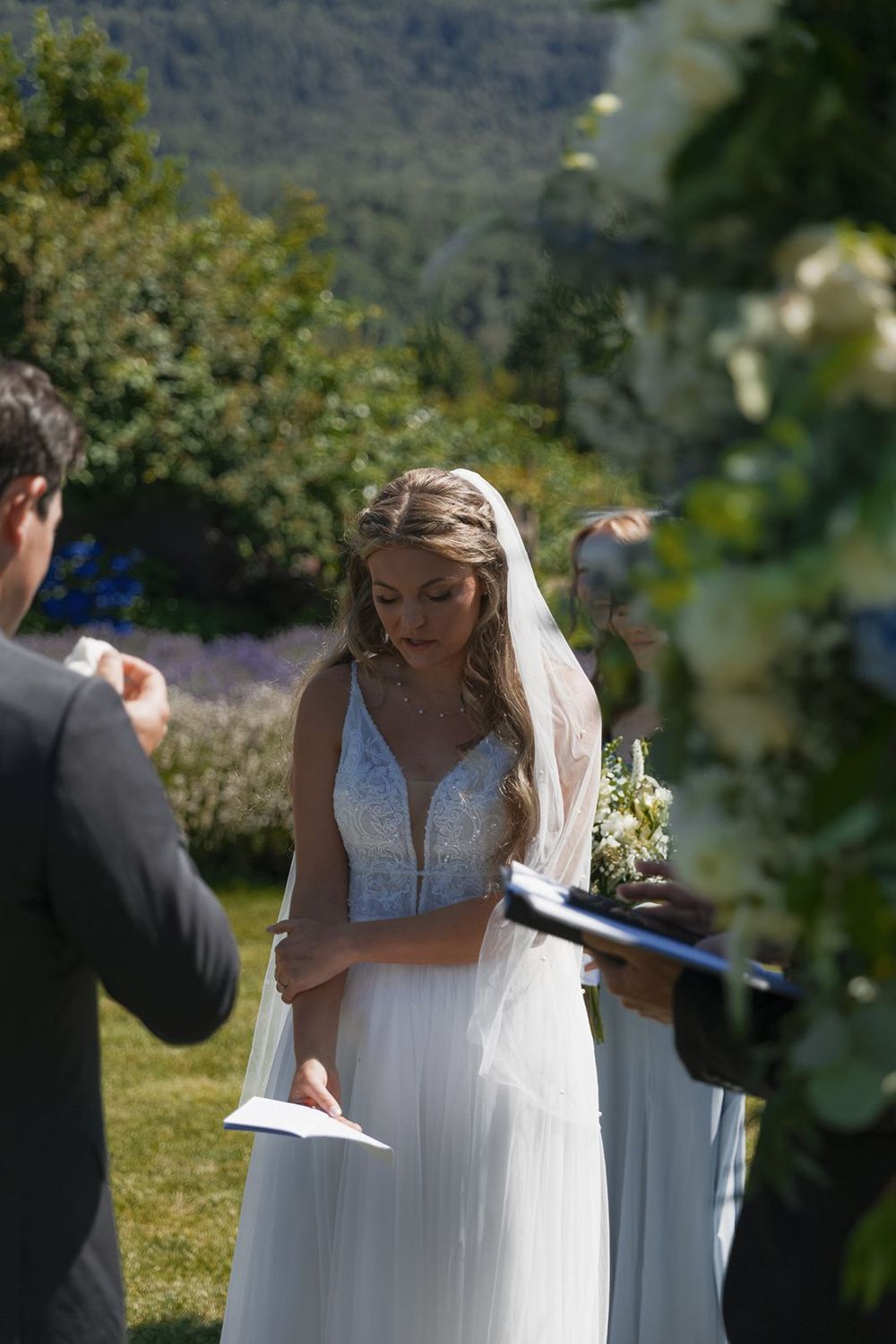 Bride reading vows at outdoor wedding ceremony in lush garden setting.