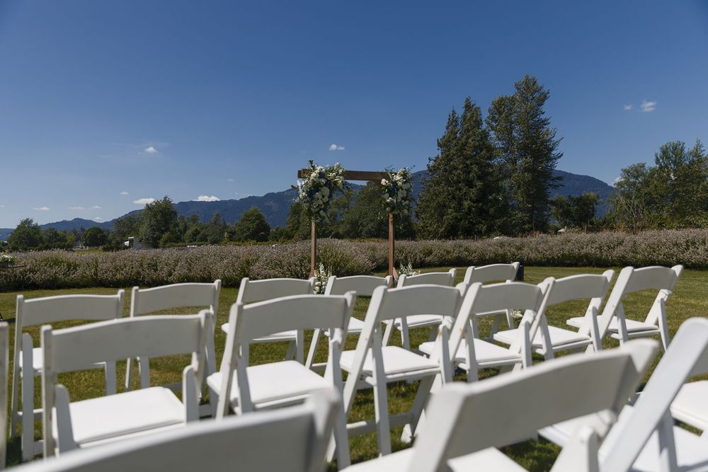 Rows of white folding chairs set up for outdoor wedding ceremony with wooden floral arch and mountain views behind.