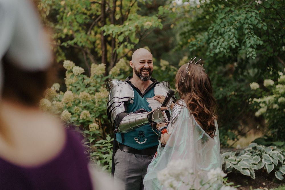 Smiling groom in medieval armor greeting his bride in a lush garden wedding ceremony setting.