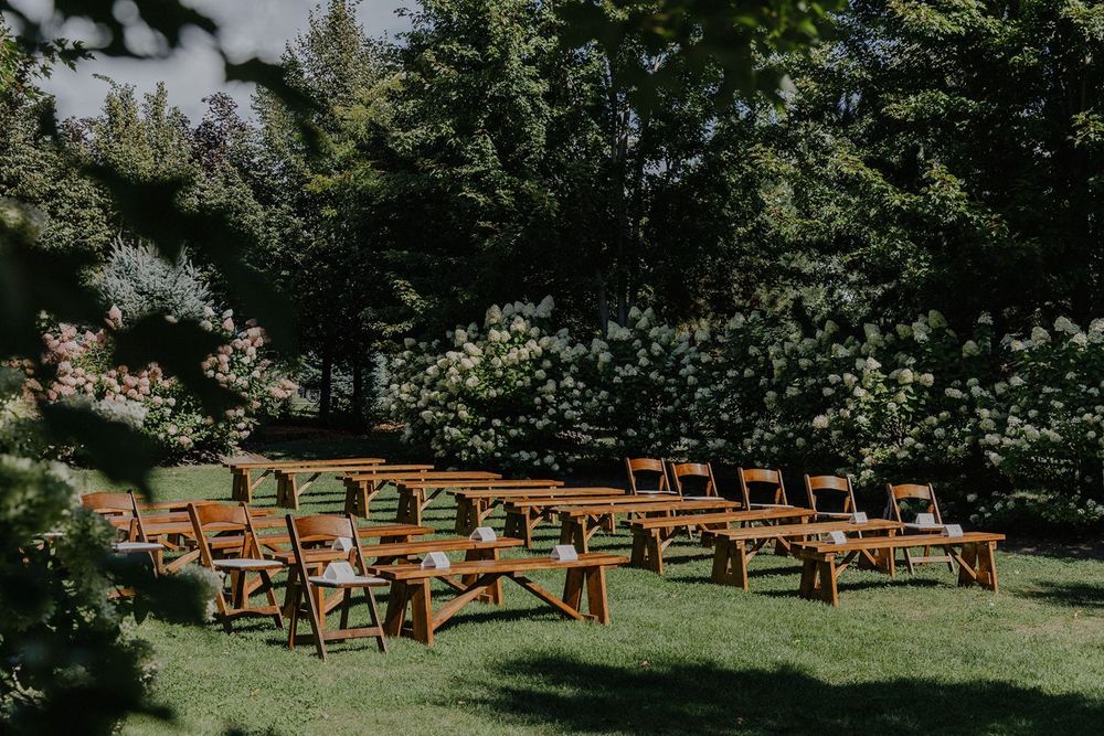 Empty wooden chairs and benches arranged on green lawn for an outdoor garden wedding ceremony.
