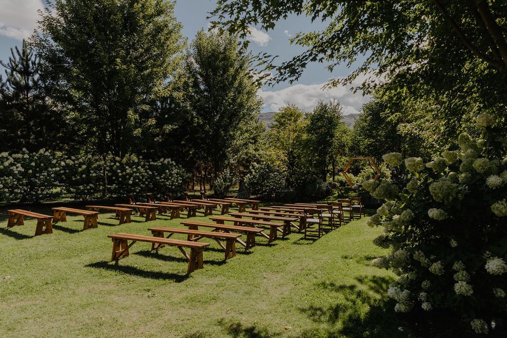 Rows of rustic wooden picnic benches arranged on green lawn for outdoor garden wedding ceremony.