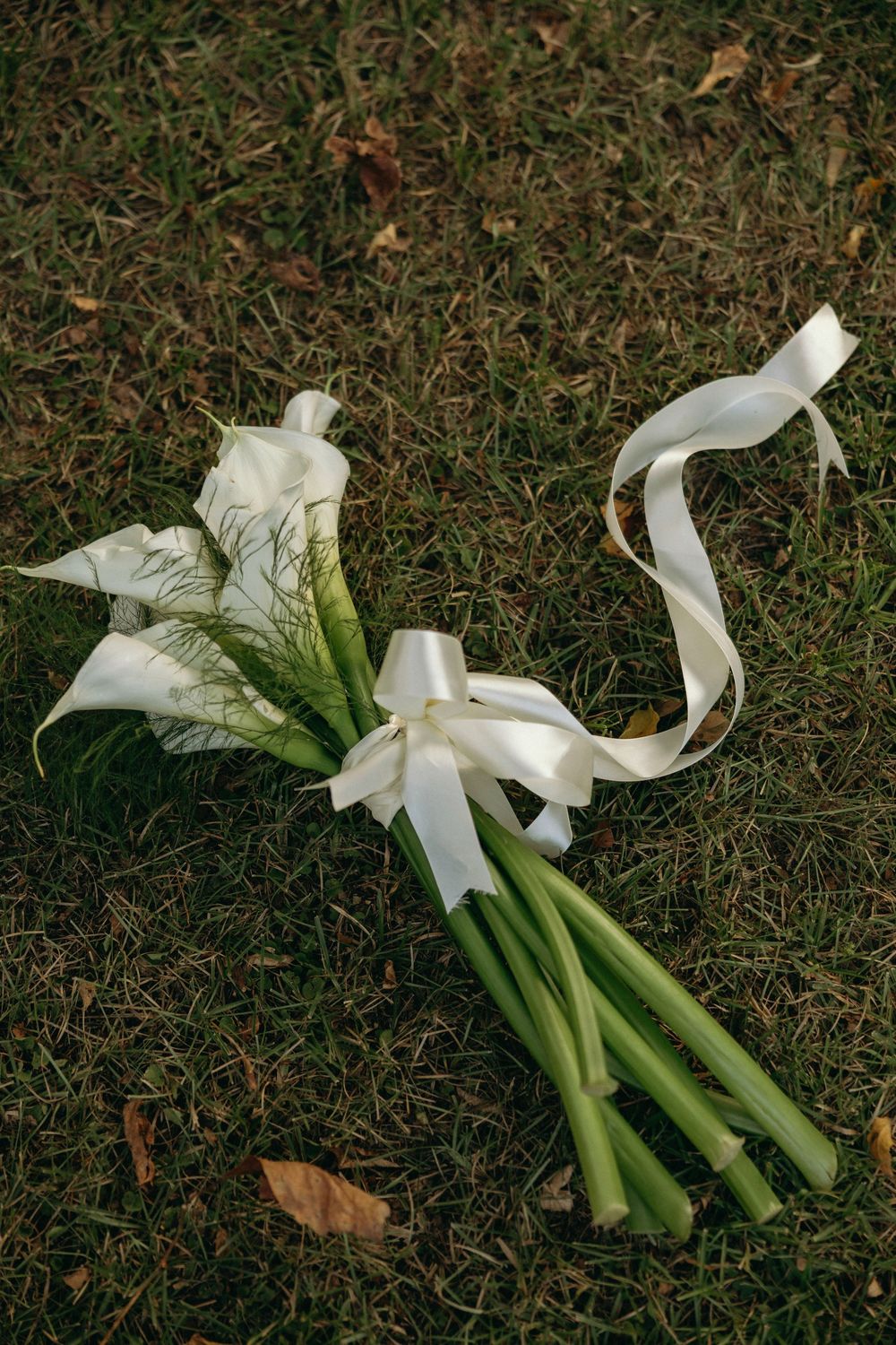White calla lily bouquet with long stems laying on grass from different angles at The Elms of Coosada in Coosada, Alabama