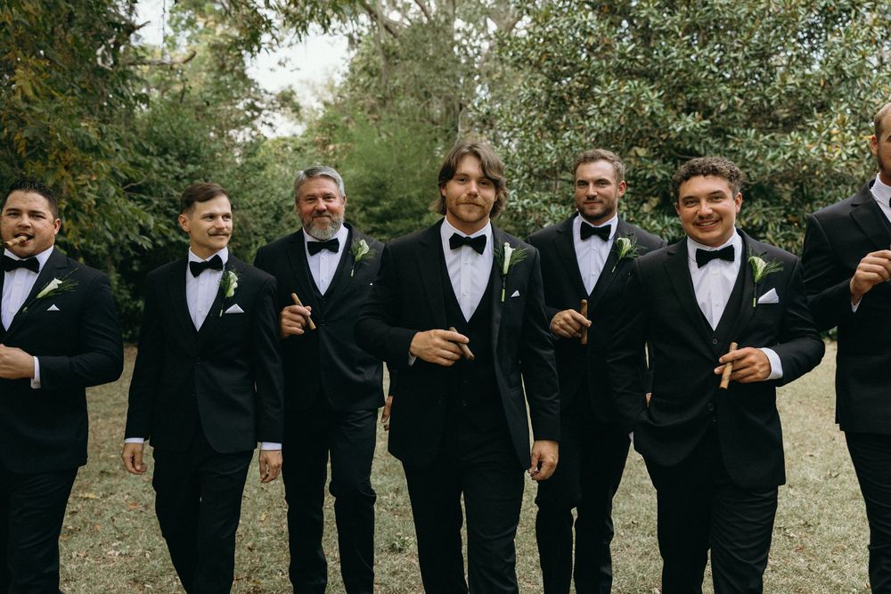Groomsmen in black tuxedos raise champagne glasses for a celebratory toast at an outdoor wedding at The Elms of Coosada in Coosada, Alabama