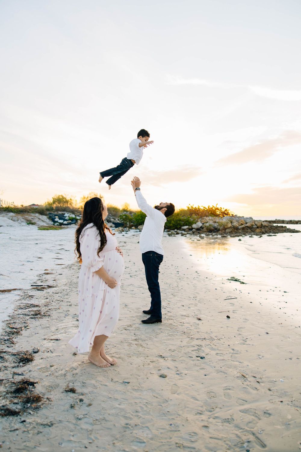 Parents lifting their child during a playful family photography session on the beach.
