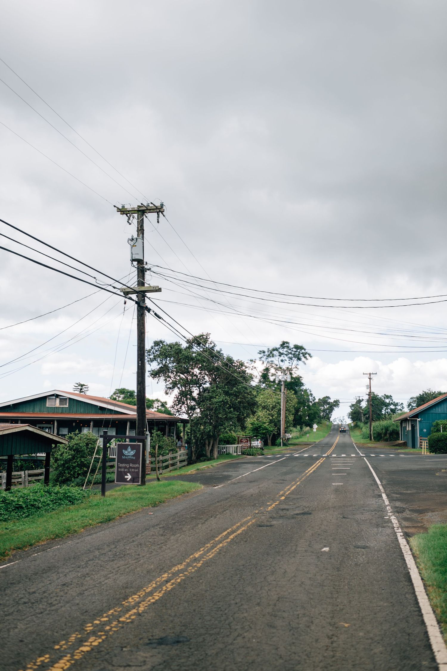 Rural road winding uphill with utility poles and yellow lines under cloudy skies.
