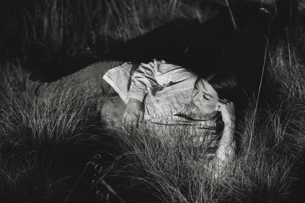 Black and white photo of pregnant woman resting peacefully in tall grass during outdoor maternity session.