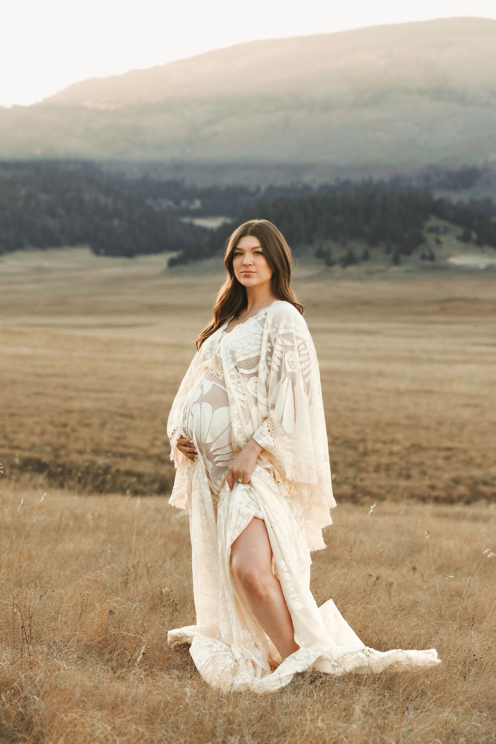 Santa Fe maternity session in sheer white lace boho maternity gown posing in golden field with mountain views.