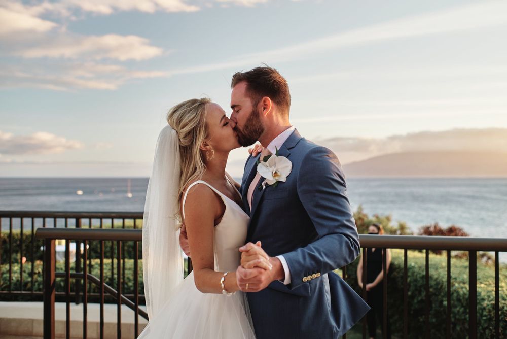 Romantic sunset moment between newlyweds on tropical balcony overlooking ocean.