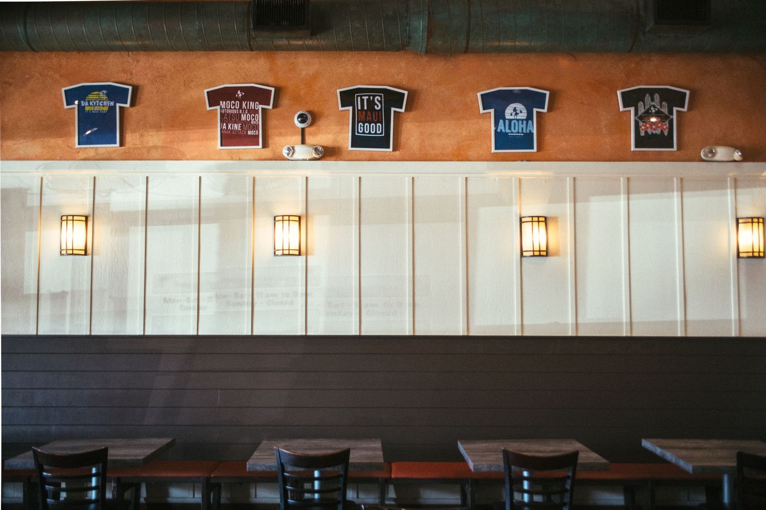 Sports jerseys displayed on orange wall with pendant lighting in restaurant.