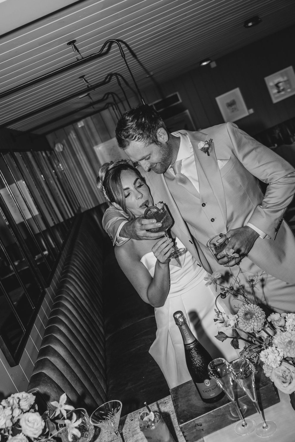 Bride and groom sharing a relaxed moment together on a banquette at Gara Rock, enjoying cocktails and champagne during their wedding day.