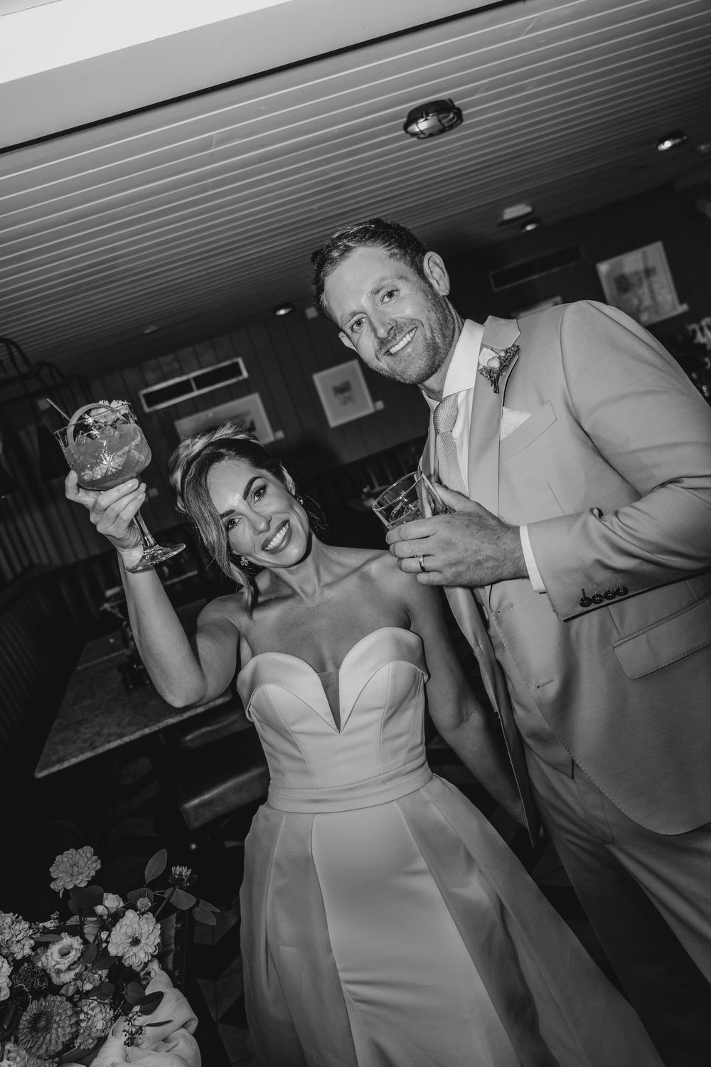 Bride and groom smiling and raising drinks in celebration inside Gara Rock, captured in a relaxed, editorial wedding portrait.