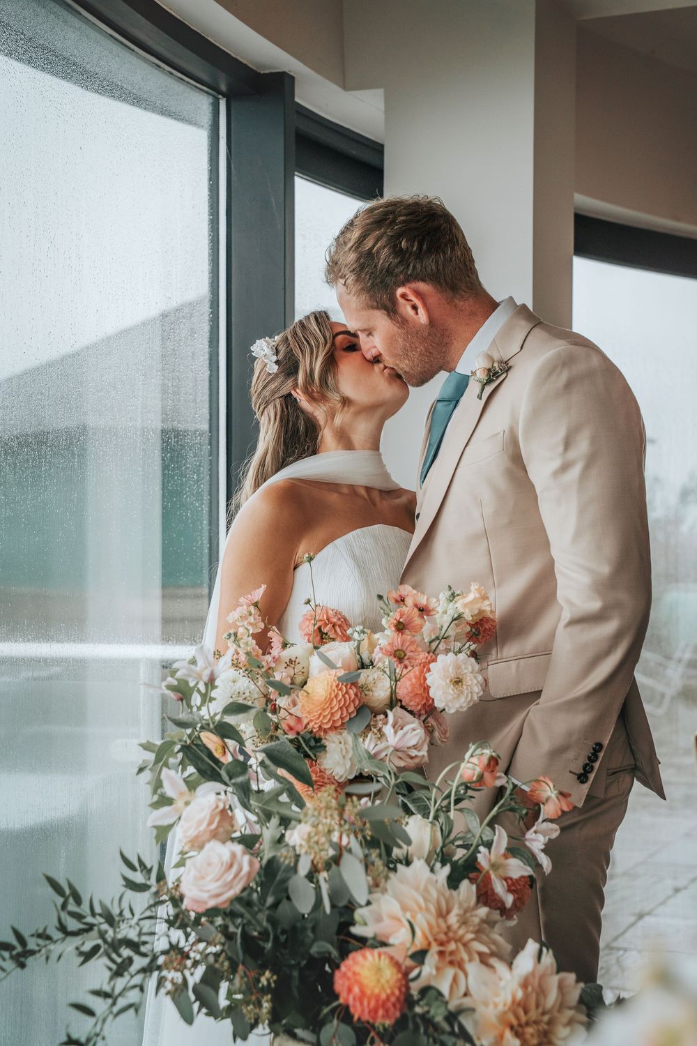 Bride and groom sharing a romantic kiss during a styled wedding ceremony at Gara Rock Hotel, surrounded by soft autumn florals and misty coa