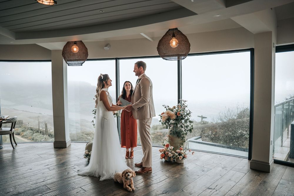 Styled wedding ceremony at Gara Rock Hotel with celebrant officiating as the bride and groom hold hands, their dog included, and panoramic c