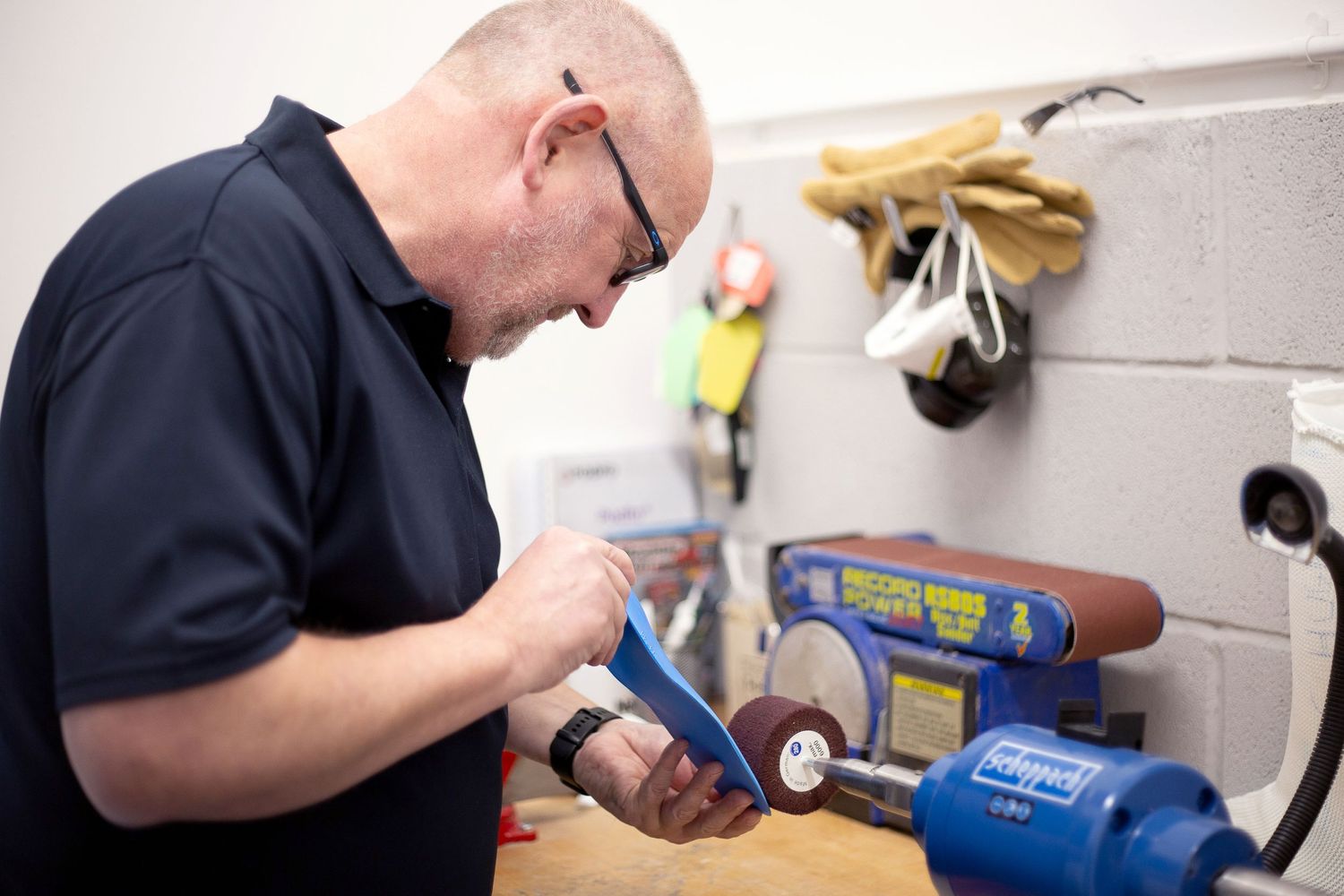 Technician in dark shirt repairing equipment at workbench with tools visible in background.