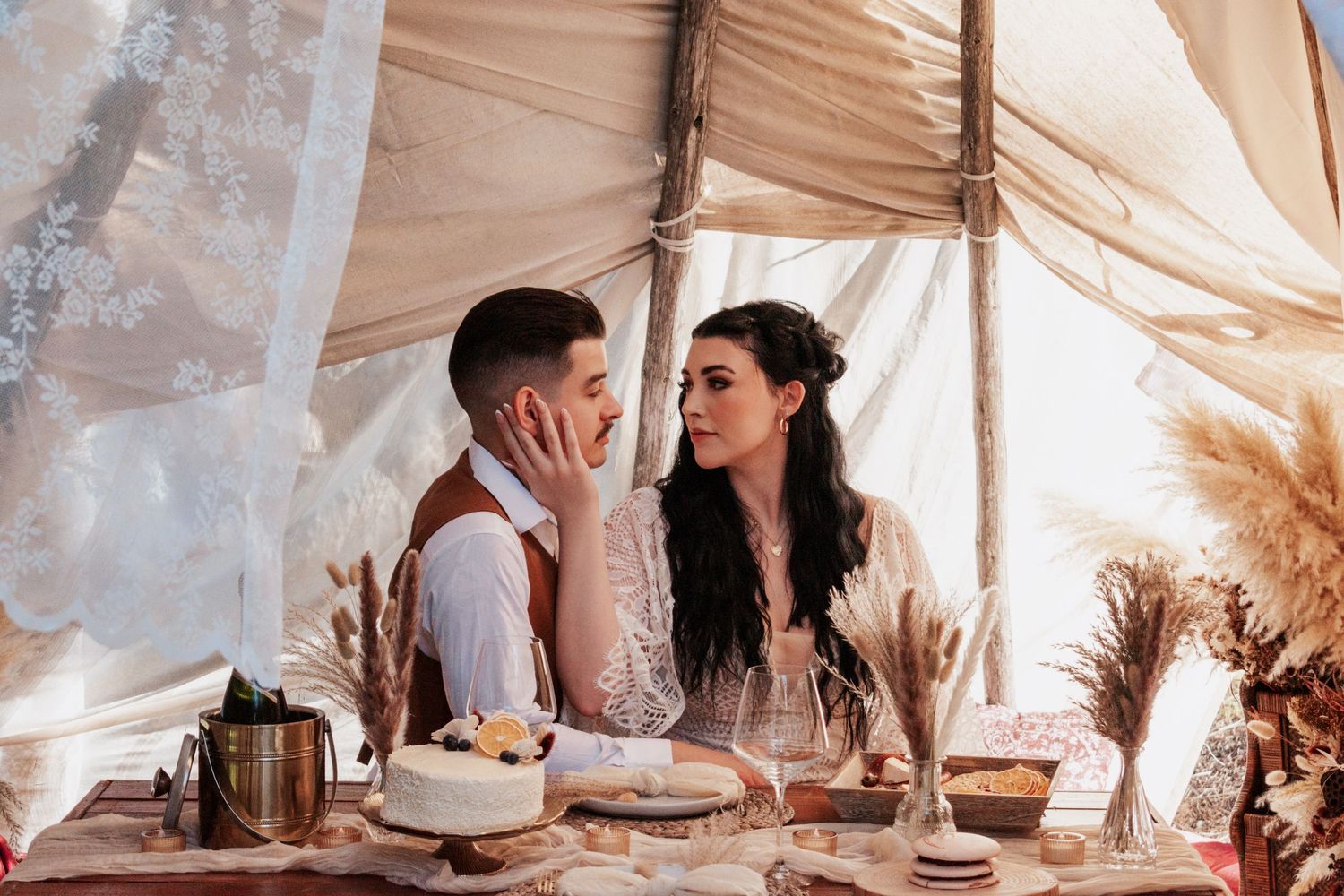 A cozy indoor engagement session featuring a couple sharing a rustic picnic setup with dried florals and warm earth-toned details in a boho-