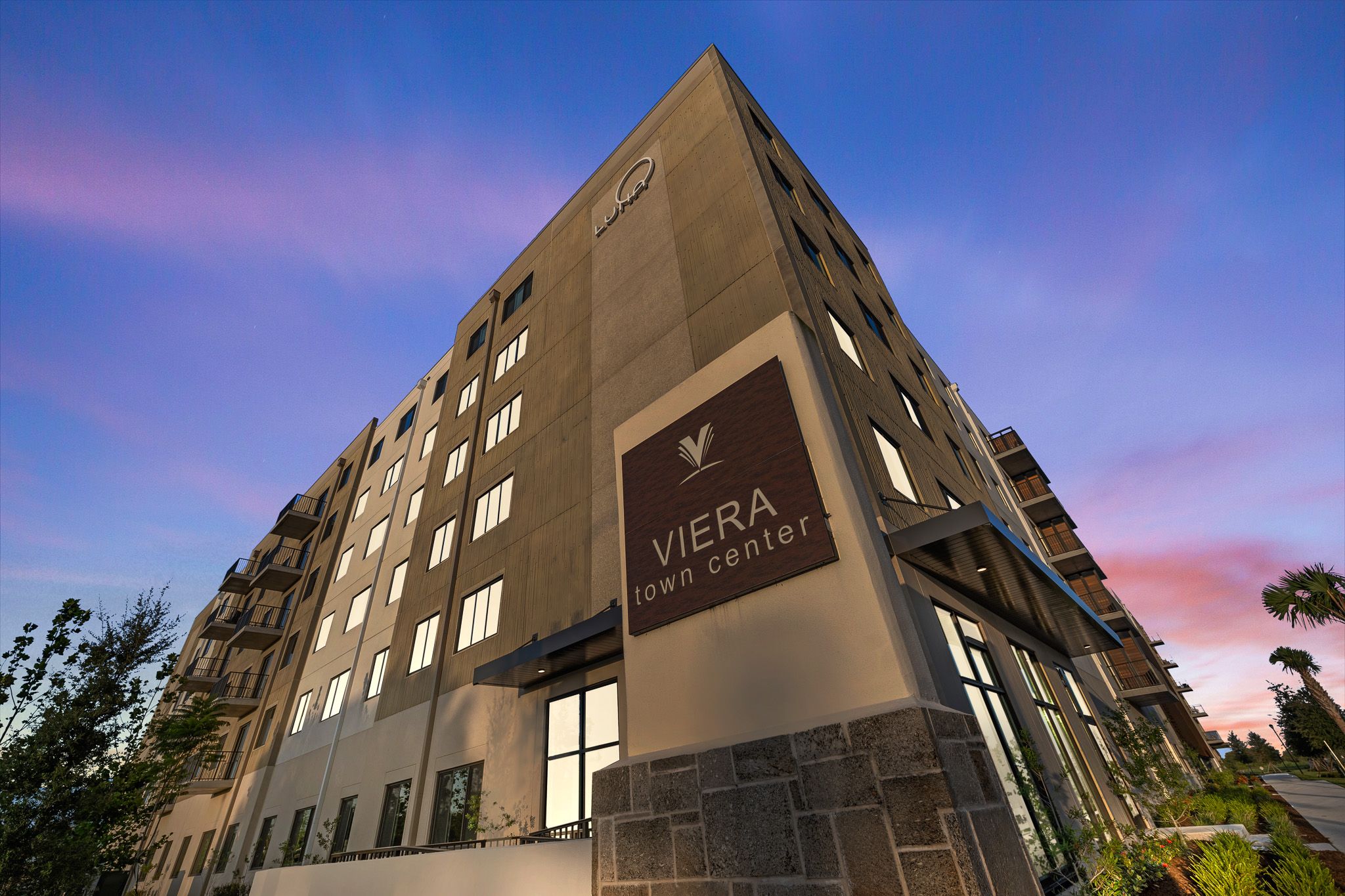 Luxury apartment building Viera exterior with illuminated signage at dusk against a purple twilight sky.