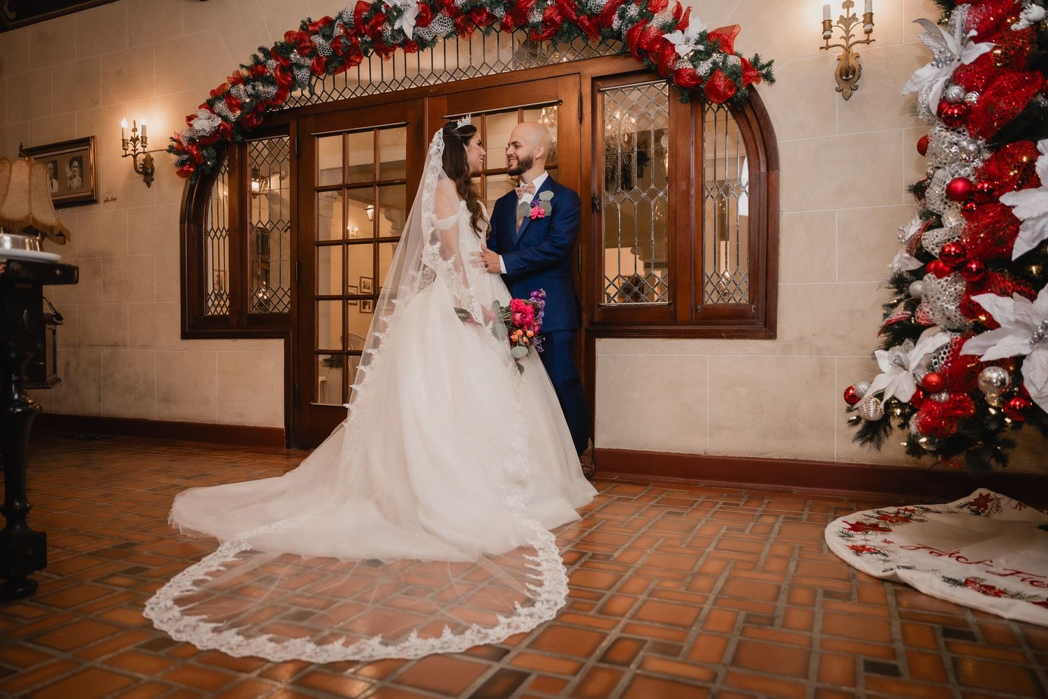 A couple dancing in a reception hall decorated for Christmas with a red and white floral archway and poinsettia tree.