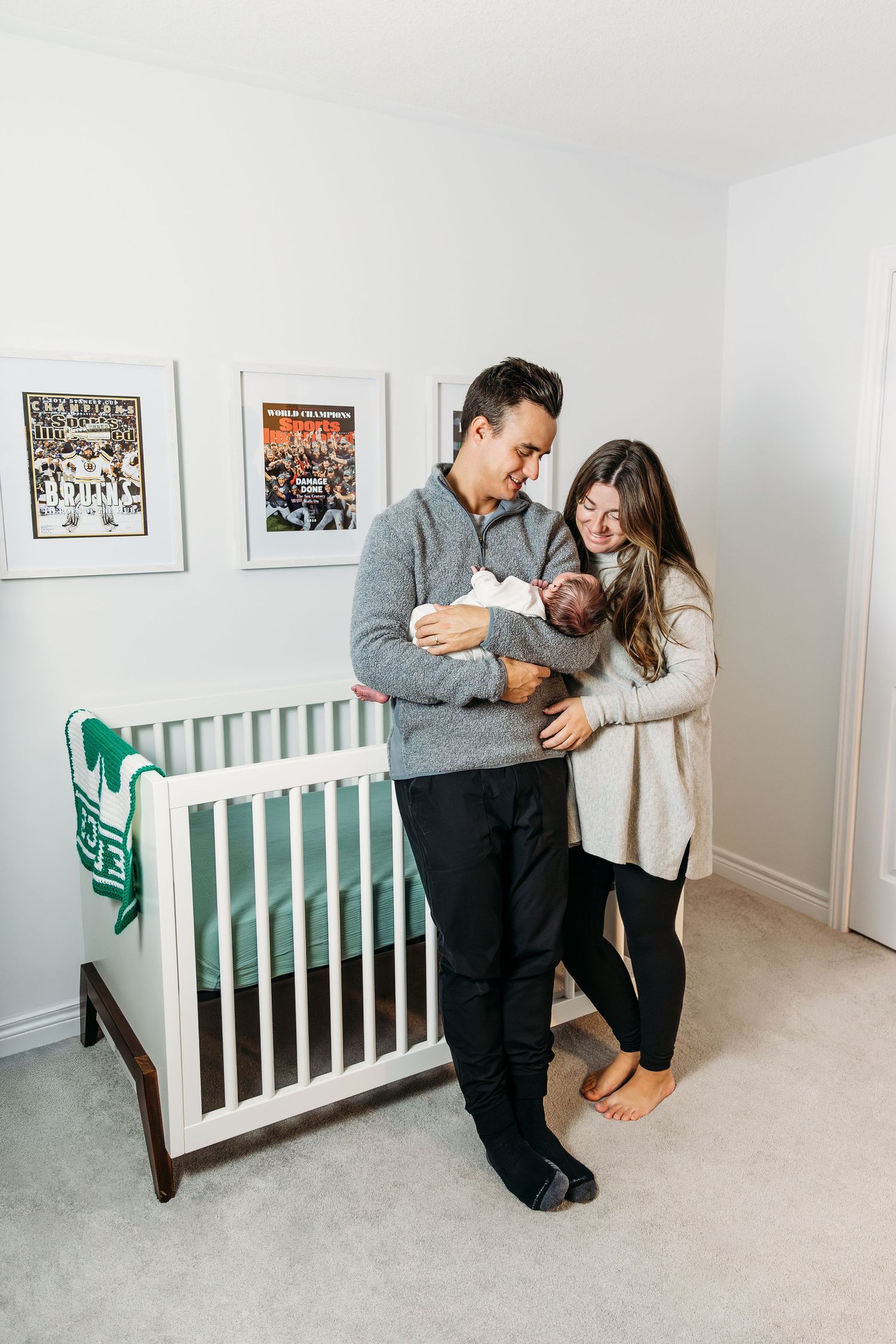 Happy family looking at  their new baby boy with love, standing in nursery in front of crib