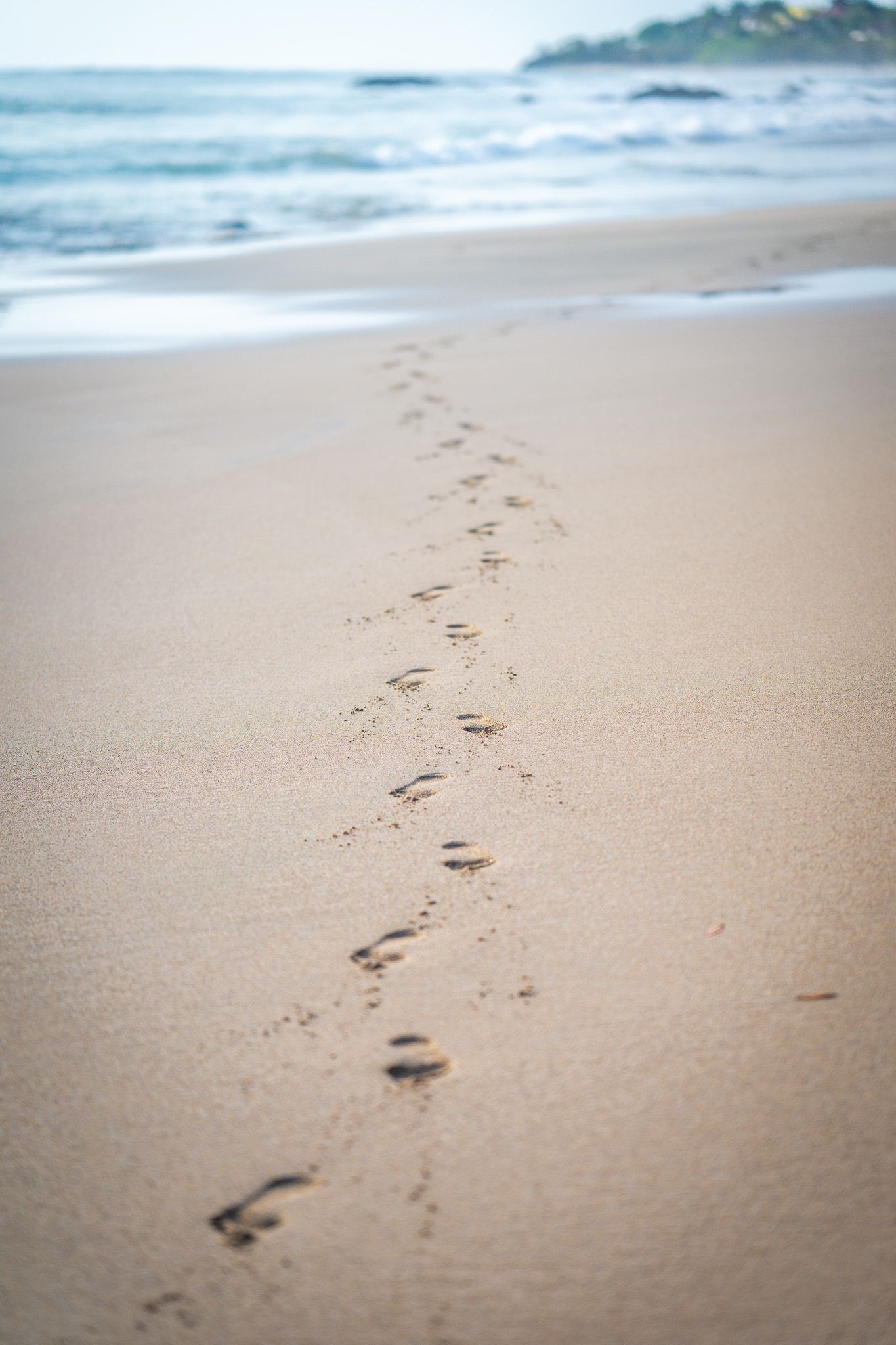 A trail of footprints meanders along the sandy beach by the ocean shore in soft focus.