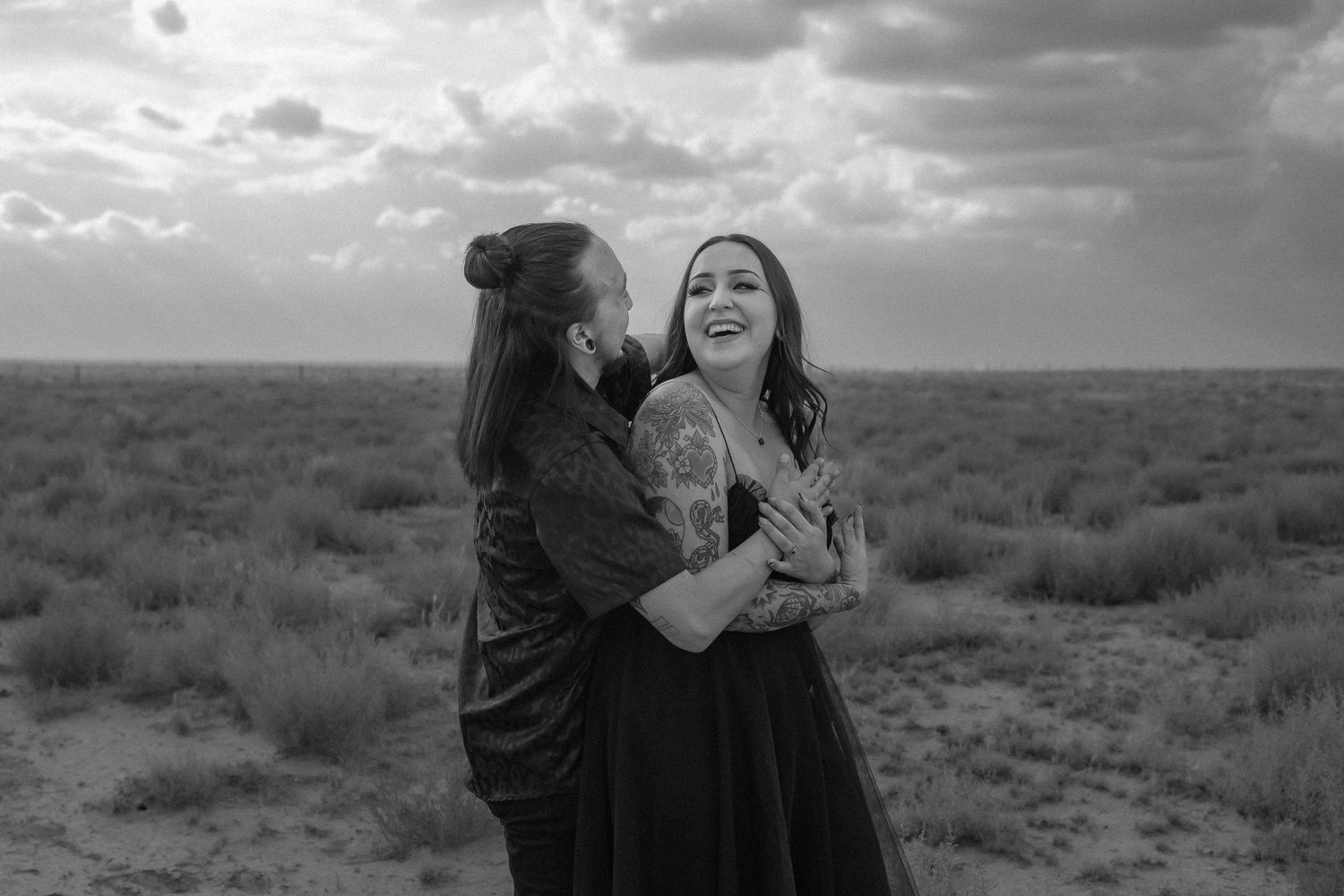 A joyful black and white moment shared in a desert landscape under dramatic cloudy skies. Albuquerque couples photographer. LGBT wedding abq