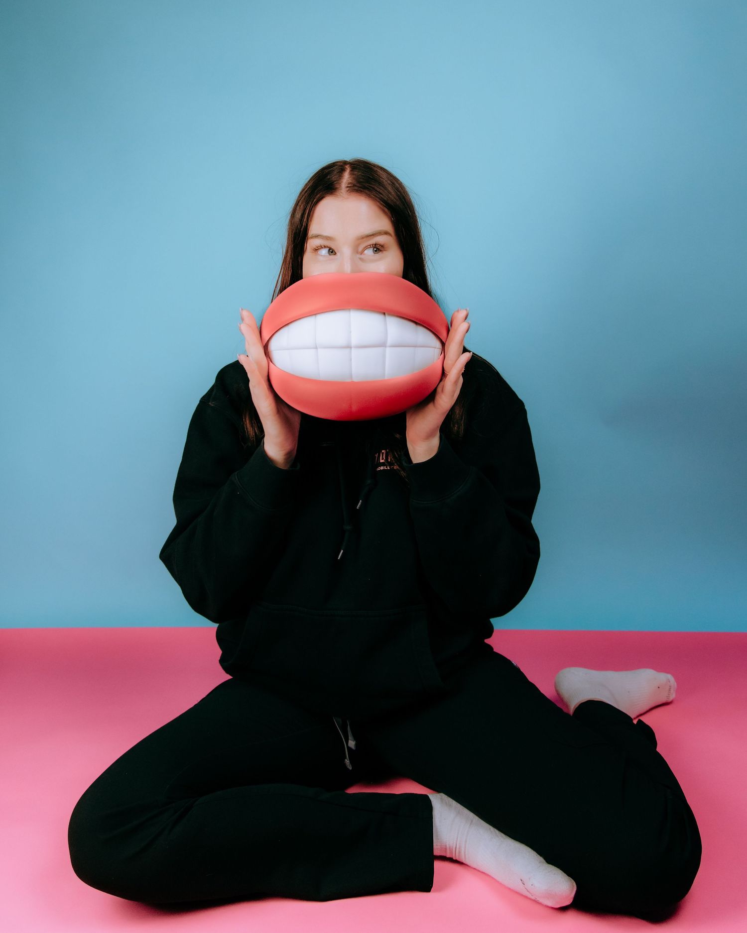 Person in black holding large decorative smiling mouth prop against blue background.