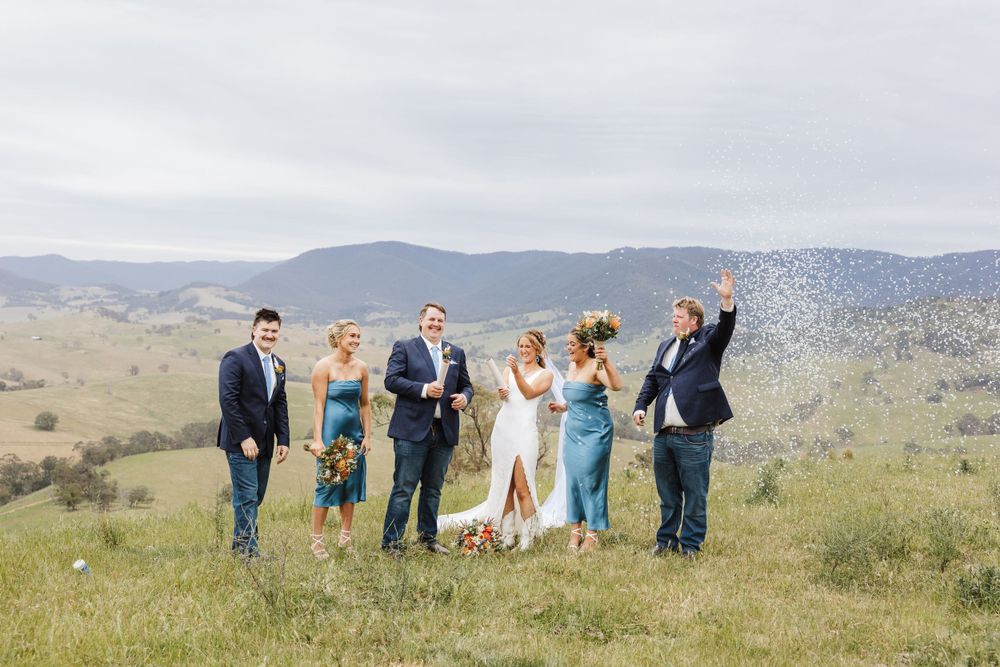 Wedding party celebrating on a hilltop with confetti against mountain backdrop.