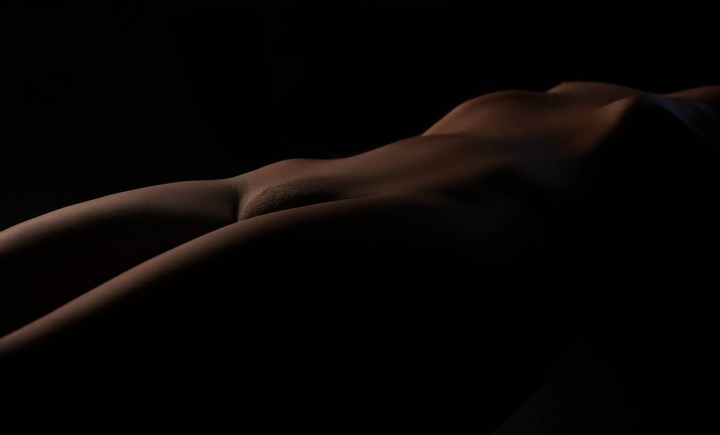 Abstract low-light fine art nude highlighting the elegant curve of a woman's hip and abdomen.