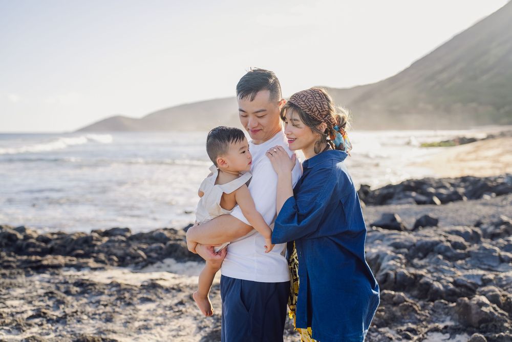 Family enjoying a romantic sunset photoshoot on a rocky beach with mountains in the background.